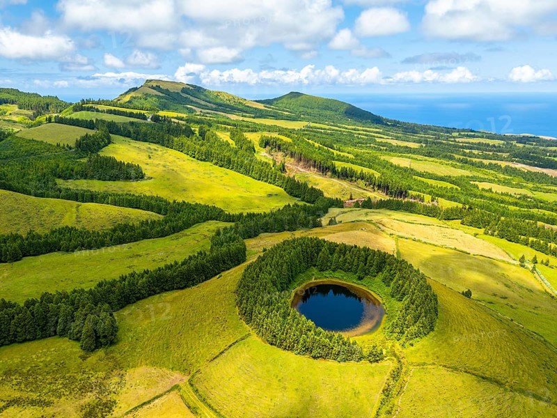 Lake Pau Pique and Lush Green Hills with Pastureland and Trees. Shadows of Clouds. Atlantic Ocean. Azores, Sao Miguel Island. Portugal. Aerial Drone Shot