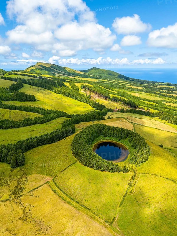 Pond Pau Pique and Lush Green Hills with Pastureland and Trees. Shadows of Clouds. Atlantic Ocean. Azores, Sao Miguel Island. Portugal. Aerial Drone Shot