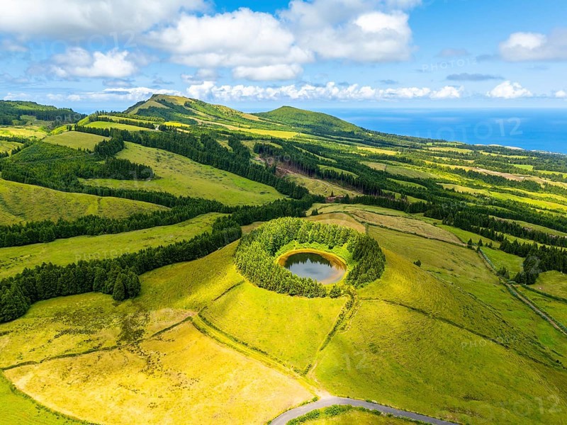 Pond Pau Pique and Lush Green Hills with Pastureland and Trees. Shadows of Clouds. Atlantic Ocean. Azores, Sao Miguel Island. Portugal. Aerial Drone Shot