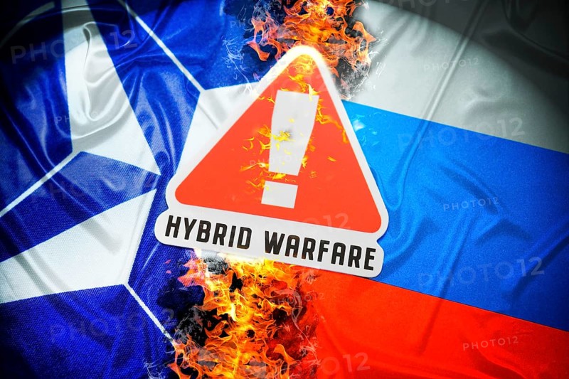 The flags of NATO and Russia with danger sign and inscription Hybrid Warfare, symbolic photo of hybrid warfare, photomontage
