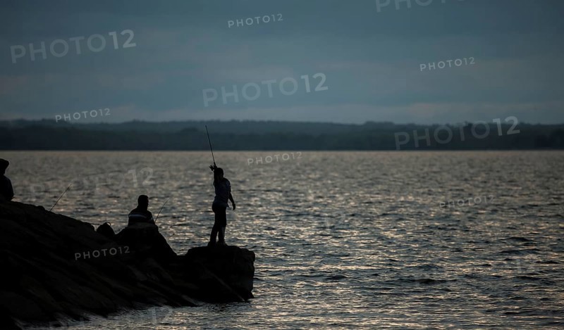 A person fishing on a rocky shore at dusk with a calm lake in Ottawa, Ontario, Canada, North America