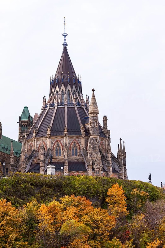 A Gothic-style Canadian Parliament building with a prominent spire, surrounded by colorful autumn foliage, highlighting historical elegance in Ottawa, Ontario, Canada, North America