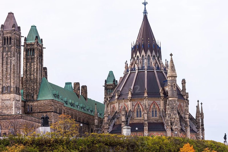 The Canadian Parliament Buildings with Gothic architecture, featuring towers and a prominent spire under a cloudy sky in Ottawa, Ontario, Canada, North America