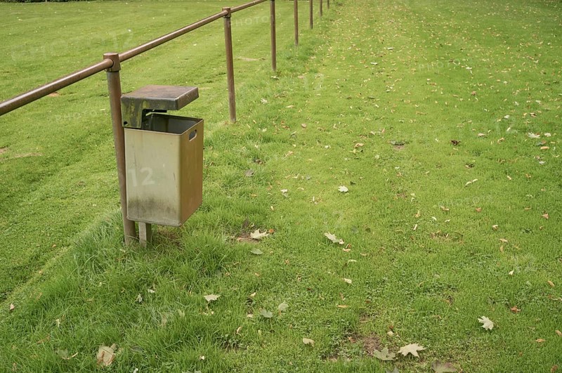 Borken, NRW, Germany, Empty metal garbage bin standing next to a railing in a public park with scattered autumn leaves