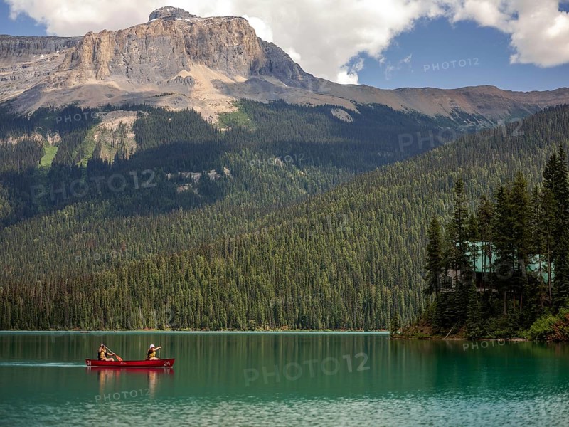 Canoe on Emerald Lake encircled by the Canadian Rocky Mountains and dense forest under a bright sky inside Yoho National Park, British Columbia, Canada, North America