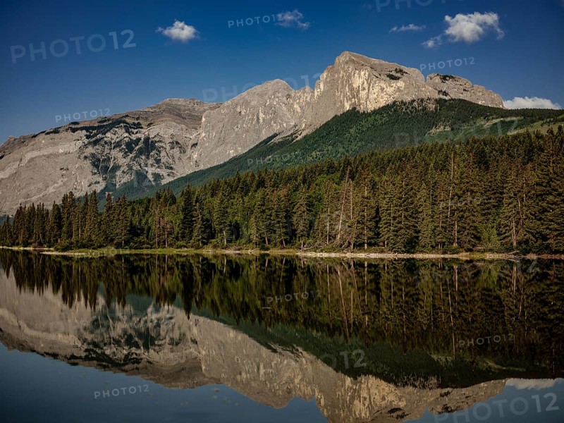Mountainous landscape of the Canadian Rocky Mountains with dense forest reflected in a calm lake near Canmore, Alberta, Canada, North America