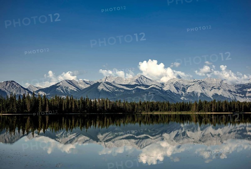 Clear reflections of mountain peaks of the Canadian Rocky Mountains in a lake under fluffy clouds near Canmore, Alberta, Canada, North America