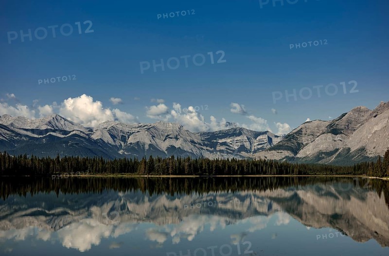 A pristine lake reflecting cloud-capped mountains of the Canadian Rocky Mountains and a peaceful forest near Canmore, Alberta, Canada, North America
