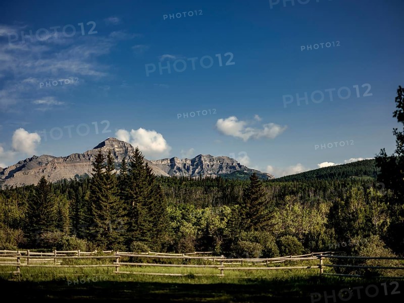 Landscape of mountains of the Canadian Rocky Mountains viewed from a grassy field with a wooden fence near Canmore, Alberta, Canada, North America