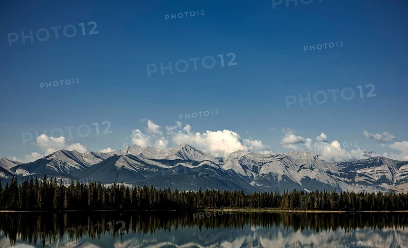 Majestic mountain range of the Canadian Rocky Mountains mirrored in a tranquil lake under a vast blue sky near Canmore, Alberta, Canada, North America