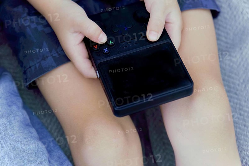 Child's hands holding and playing portable video game console, enjoying entertainment
