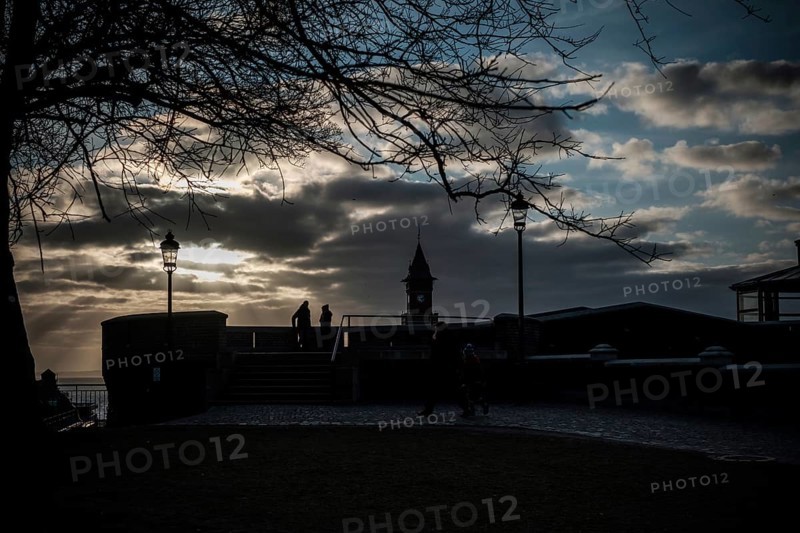 Figures silhouetted against sunset with dramatic clouds, tree, and lampposts in Helsingborg, Sweden, Scandinavia, Northern Europe