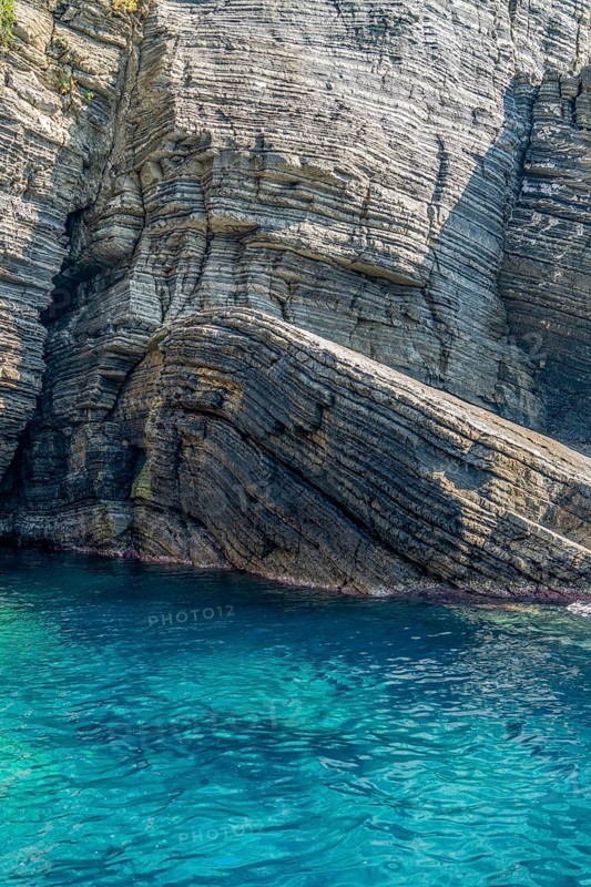 Sunny illuminated detail of the ligurian coast showing a layered rock formation and blue sea