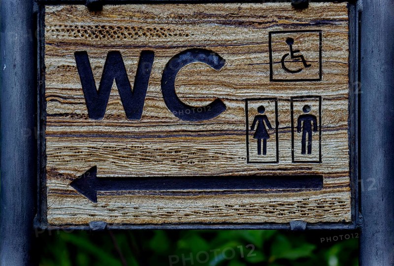 Wooden sign indicating direction of public toilet facilities for all users in ronda, malaga, spain