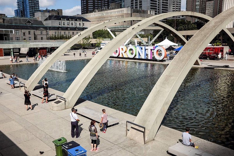 Public plaza in Toronto with arches over a fountain and people enjoying the sunny day in Toronto, Ontario, Canada, North America