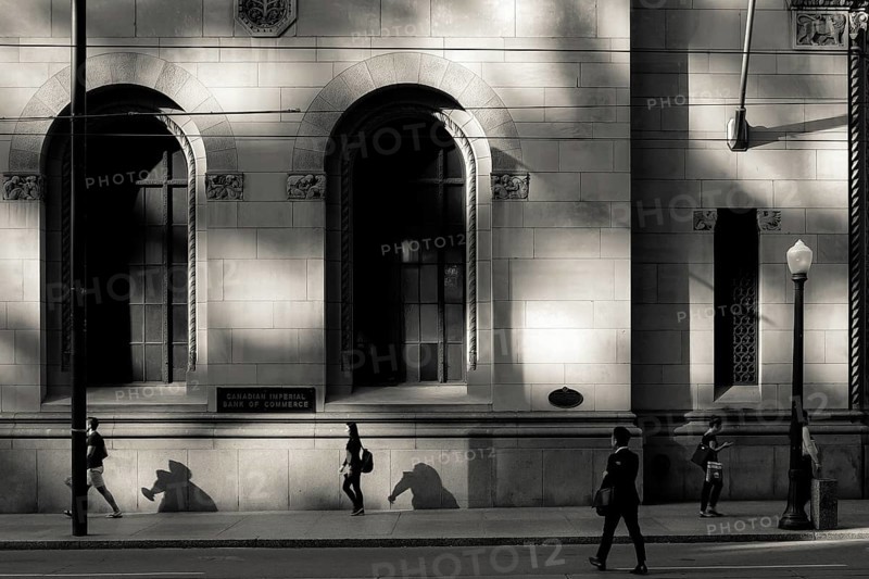 Black and white urban scene with people walking past a sunlit building casting strong shadows in Toronto, Ontario, Canada, North America