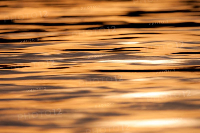 Calm water with ripples reflecting a warm orange sunset, creating a peaceful atmosphere in Muskoka, Ontario, Canada, North America