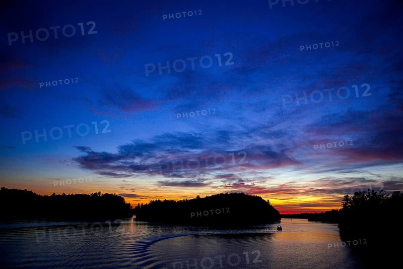 Boat sails on a serene lake during sunset, creating a vivid twilight sky in Muskoka, Ontario, Canada, North America