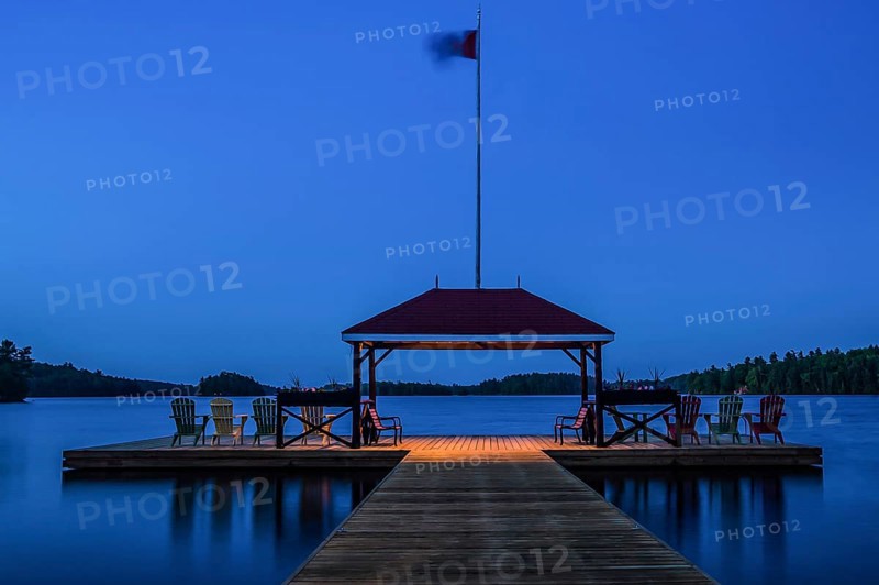 A tranquil lakeside dock with chairs and a flag at dusk in Muskoka, Ontario, Canada, North America