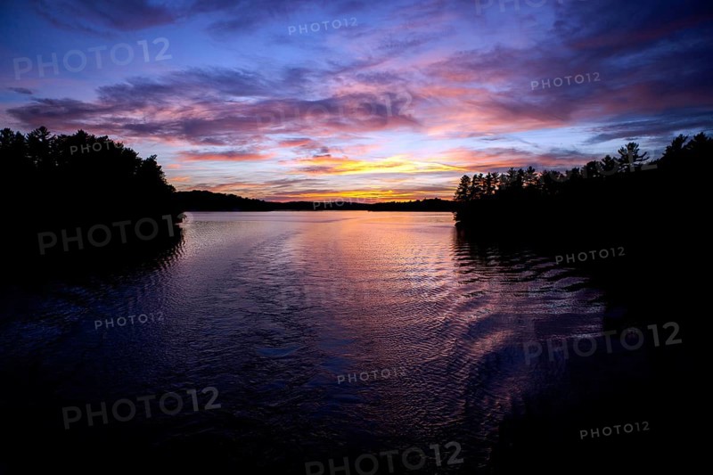 Calm water reflects a colorful evening sky, creating a peaceful twilight landscape in Muskoka, Ontario, Canada, North America