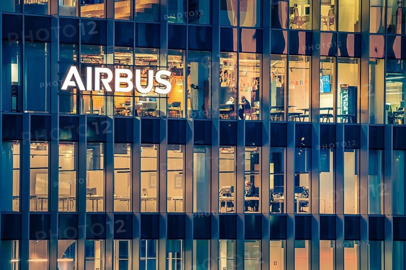 Jan 15, 2025 - Lisbon, Portugal: Night view of the Airbus office building or headquaters with bright illuminated logo and modern glass facade. Interior of workspace with people at desks, leading aerospace company, modern architecture, daily corporate