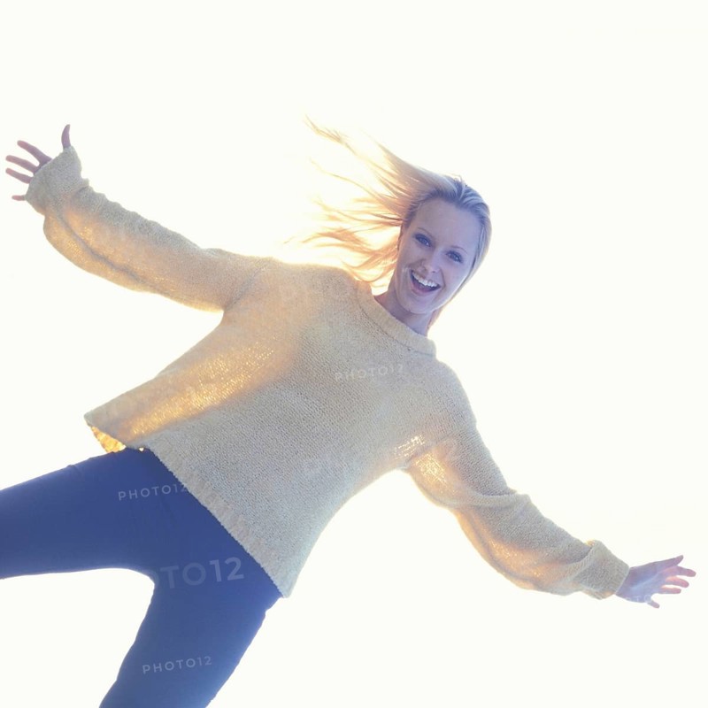 A smiling woman in casual clothes with a bright, light-filled background creating a joyful atmosphere