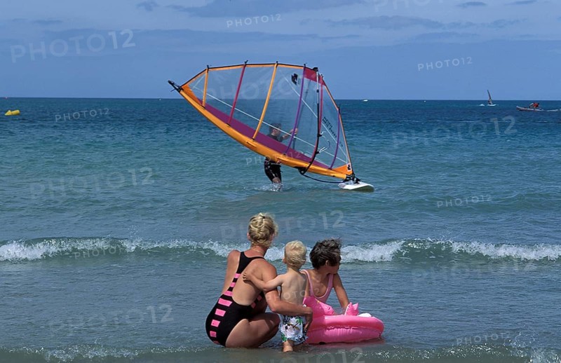 Family at the beach watching windsurfing. Two children with an adult, enjoying the sunny day