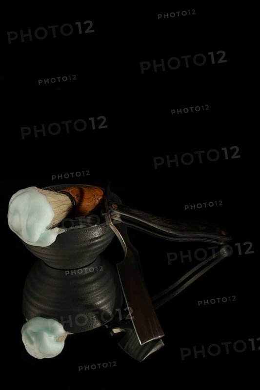 Shaving brush with cream and straight razor reflecting on a black background