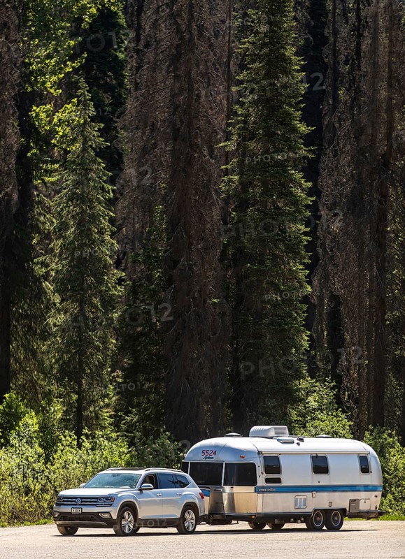 An Airstream travel trailer parked with a car by a dense forest, highlighting travel adventure in side Glacier National Park, near Selkirk, British Columbia, Canada, North America. RV parked with a car by a dense forest, highlighting travel adventure