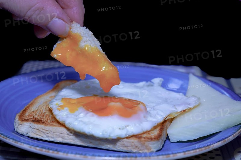 Close-up of a hand dipping bread into a runny egg yolk, served on toast with cheese, creating a delicious and simple breakfast