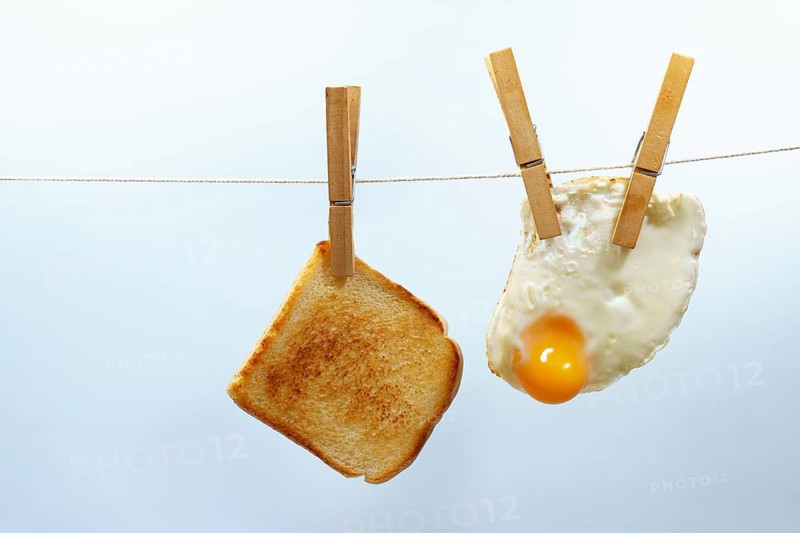Toasted bread and fried egg are hanging from a clothesline with wooden clothespins, representing a unique breakfast scenario