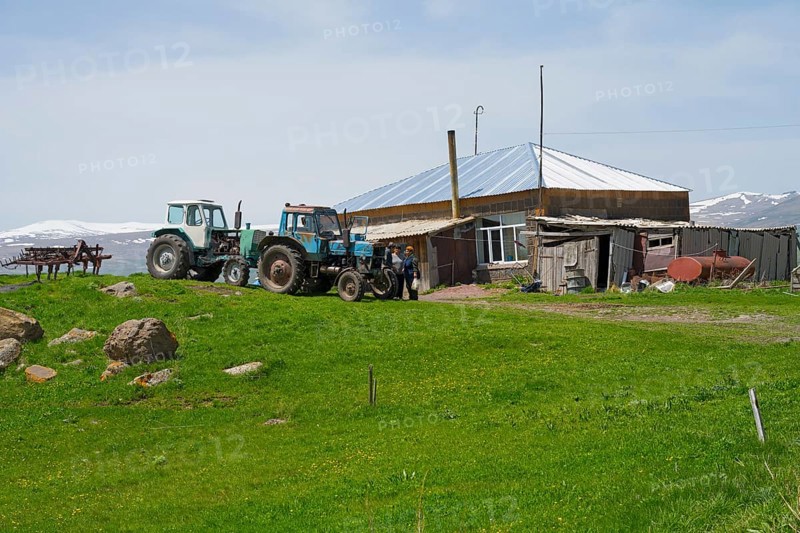 Two tractors standing on a green field next to a farmhouse and a barn, Zorakert, Lake Arpi, Shirak Province, Armenia