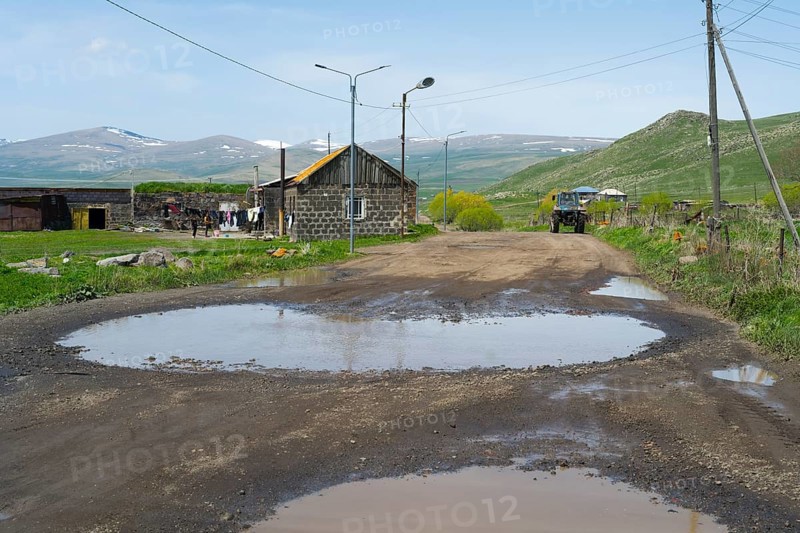 A muddy road with large puddles leads through a village with mountains in the background, Zorakert, Lake Arpi, Shirak Province, Armenia
