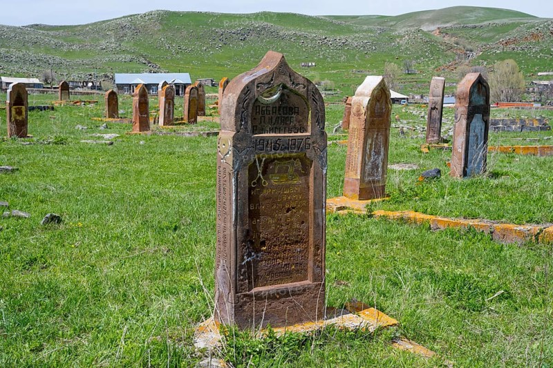 A well-preserved old gravestone on green grass in front of a hilly landscape with several gravestones, old cemetery, Aghvorik, Shirak province, Armenia