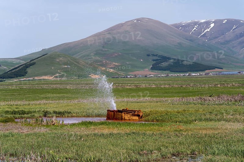 A tranquil landscape with hills and a water fountain in a green meadow, geyser near Karmravan, Shirak province, Armenia