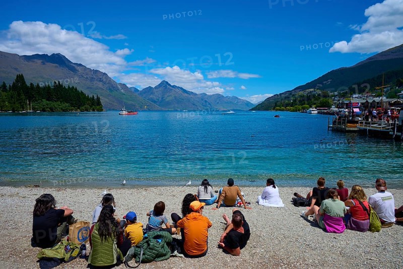 Groups of people sitting on the beach enjoying the view of the lake and mountains, Queenstown, Queenstown-Lakes District, Otago, South Island, New Zealand