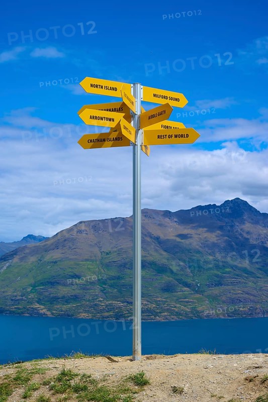 A signpost on a hill shows yellow signs in different directions, Queenstown, Queenstown-Lakes District, Otago, South Island, New Zealand