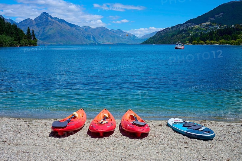 Red kayaks and paddleboard on the beach in front of a calm lake with mountain views, Queenstown, Queenstown-Lakes District, Otago, South Island, New Zealand