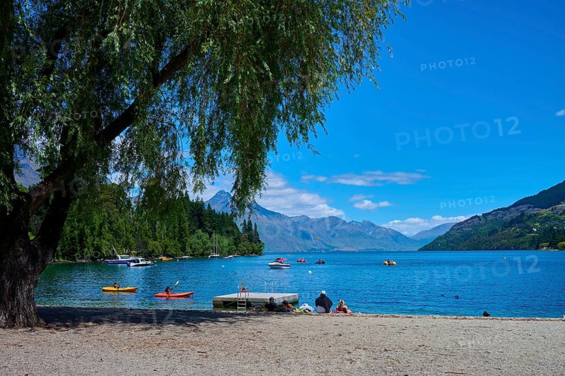 Sunny day at the lake with calm water, people relaxing on the shore and boats floating on the water, Queenstown, Queenstown-Lakes District, Otago, South Island, New Zealand