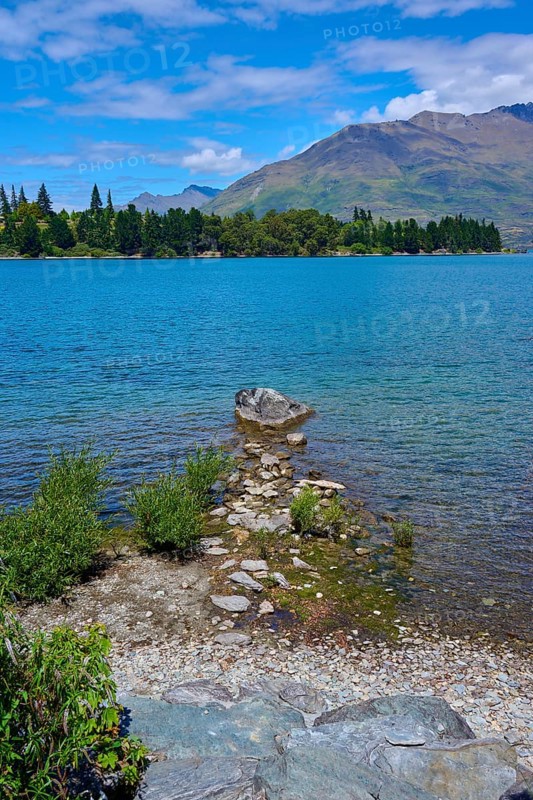 Rocks on the shore of a lake with mountains in the background and a clear atmosphere, Queenstown, Queenstown-Lakes District, Otago, South Island, New Zealand