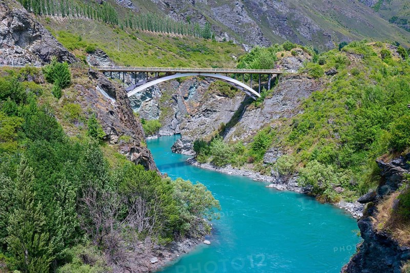 A bridge spans a turquoise-coloured river in a green and rocky landscape, Kawarau River, Queenstown, Otago, South Island, New Zealand