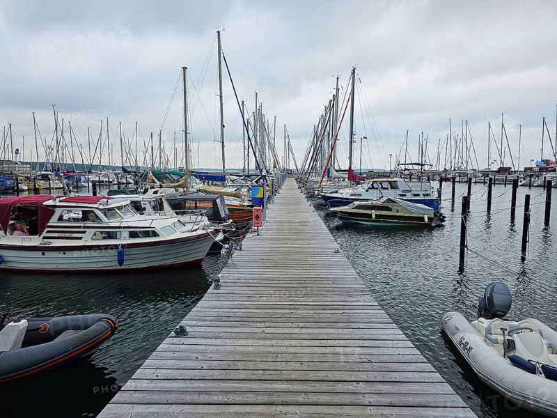 A wooden walkway leads through a harbour, lined with boats and masts under a cloudy sky, Laboe, Kiel Fjord, Schleswig-Holstein, Germany
