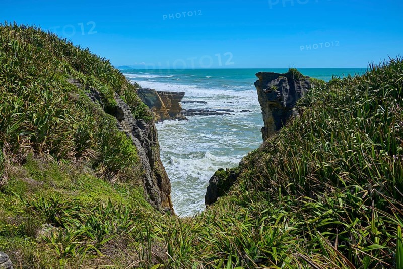 Cliff landscape with lush green vegetation and roaring sea behind the rocks, Pancake Rocks, Westport, Greymouth, West Coast, South Island, New Zealand