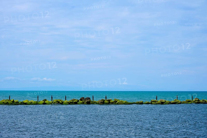 View of the sea with a row of rocks and calm blue sky, Mana Bay, Patea, Taranaki, North Island, New Zealand