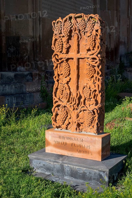 A detailed engraved red gravestone with a cross motif stands on a grassy area in the sunlight, cross stone, Khachkar, Marmashen Monastery, Marmashen Vank, Shirak Province, Armenia
