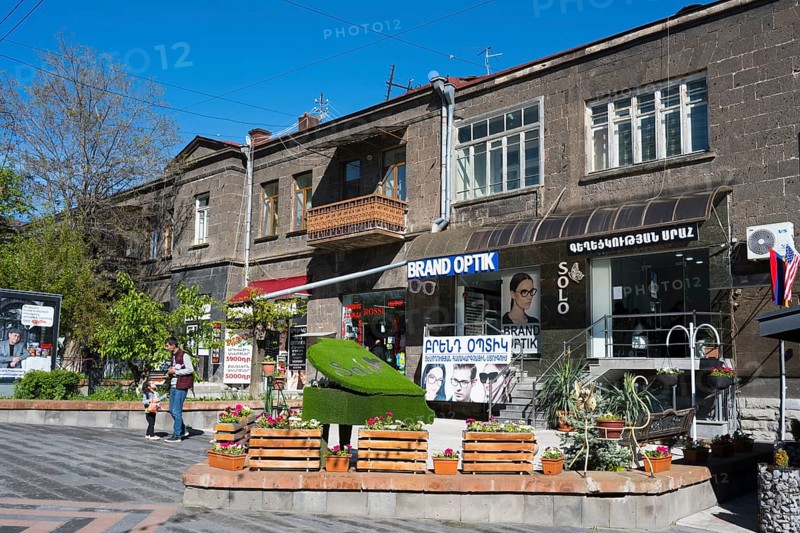 Pedestrian zone with optical shop and advertising signs, flanked by concrete buildings and trees, Gyumri, Gyumri, Shirak Province, Armenia
