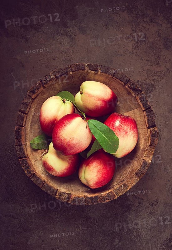 Ripe nectarine, in a wooden plate, brown background, top view, no people