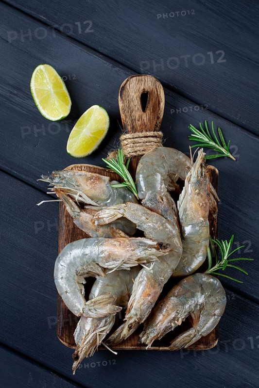 Fresh raw, white-footed shrimp, tiger prawns vannamei, on a wooden cutting board, with lime slices, and seasonings
