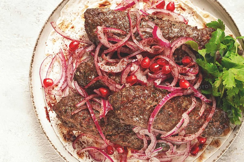 Grilled kebabs topped with onions and pomegranate on a white plate in a bright kitchen setting