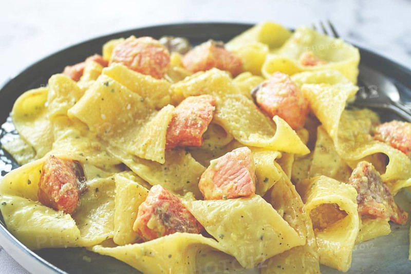 Papardelle pasta, in creamy sauce with salmon, natural light, lifestyle, homemade, on a gray background, no people